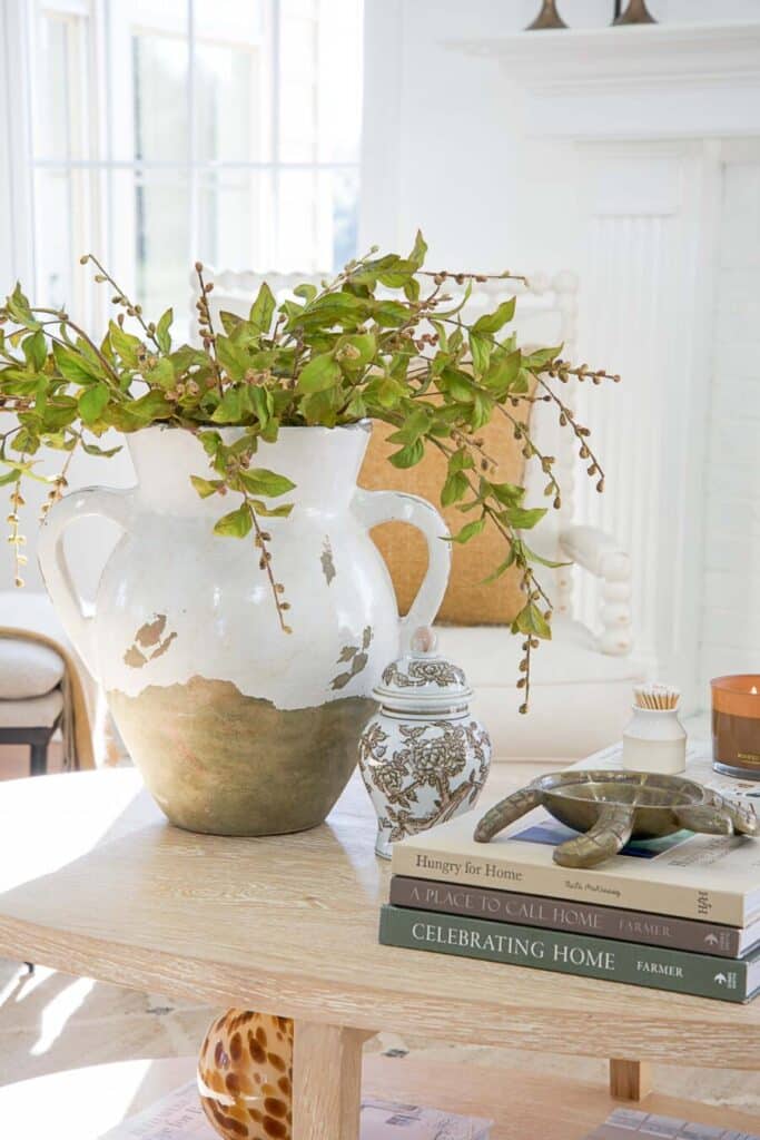 CLASSIC DECOR TRENDS- COFFEE TABLE WITH NEUTRAL ITMES AND A NEUTRAL VASE FILLED WITH GREENS