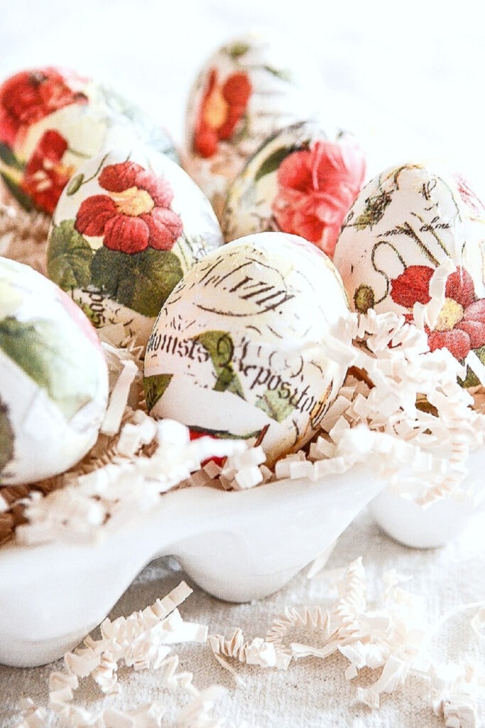 decoupaged eggs in a white ceramic egg crate with crinkle paper