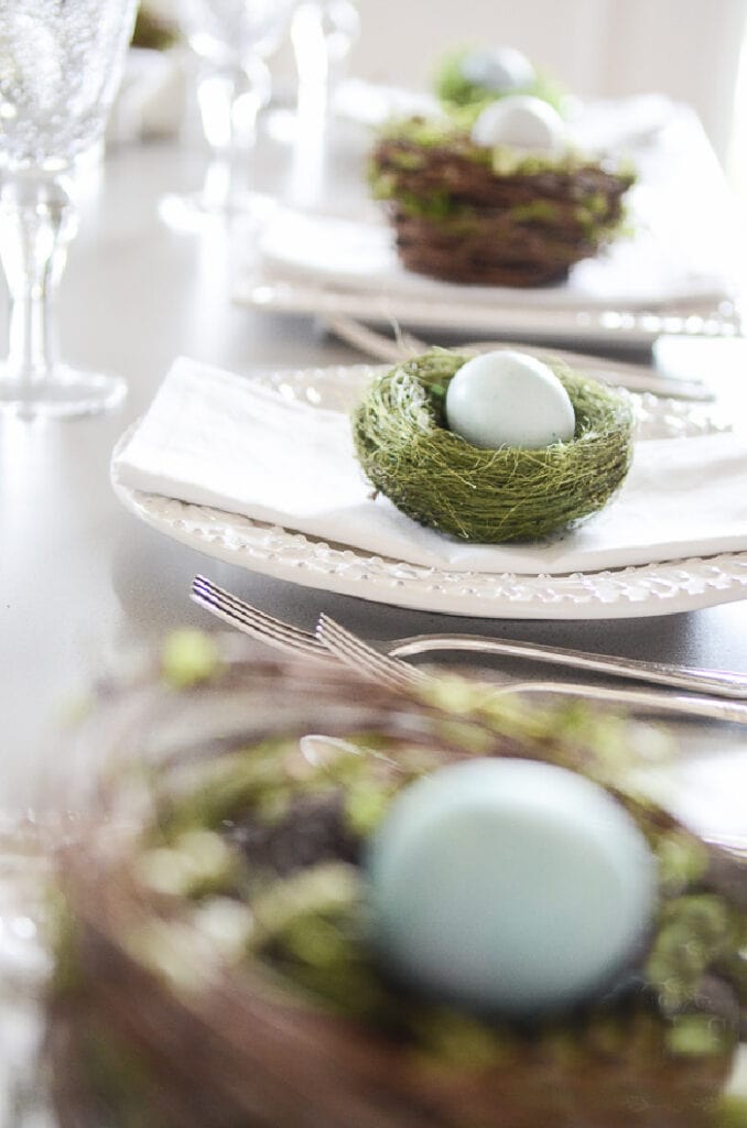 decorative nests with blue dyed eggs on each plate on an Easter table.